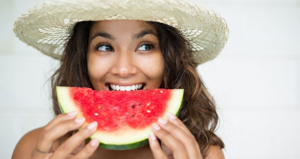 woman with straw hat holding watermelon slice to mouth