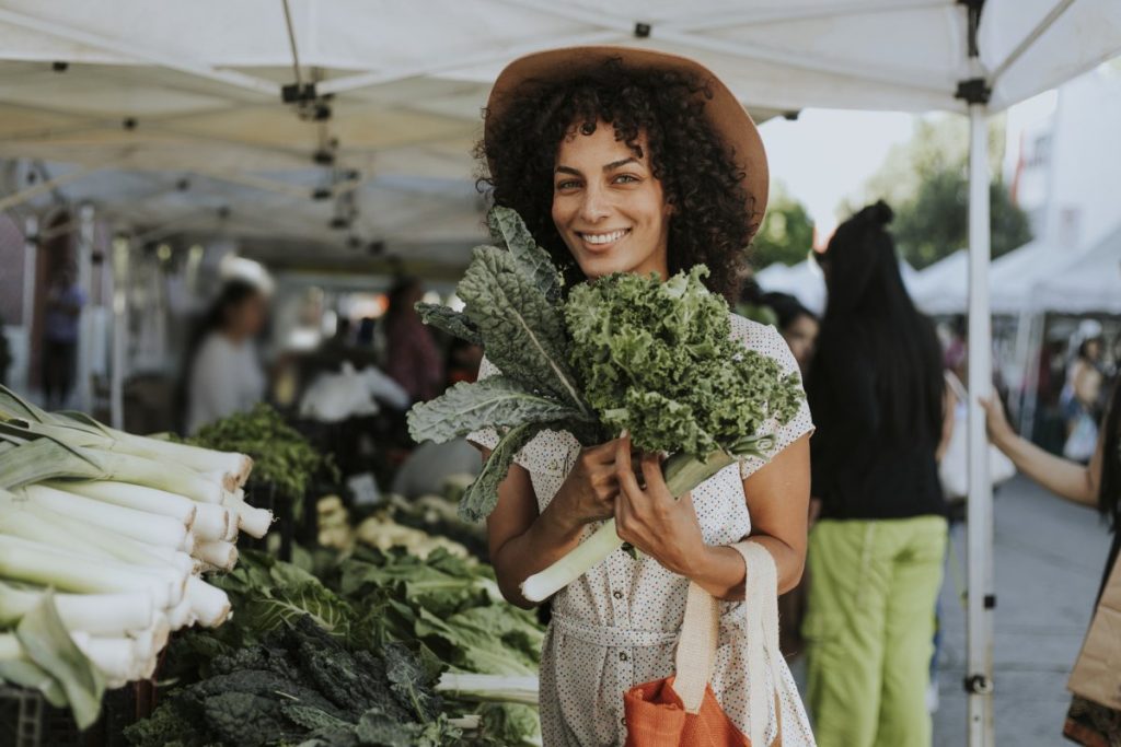 Woman of color purchasing kale from a farmers' market