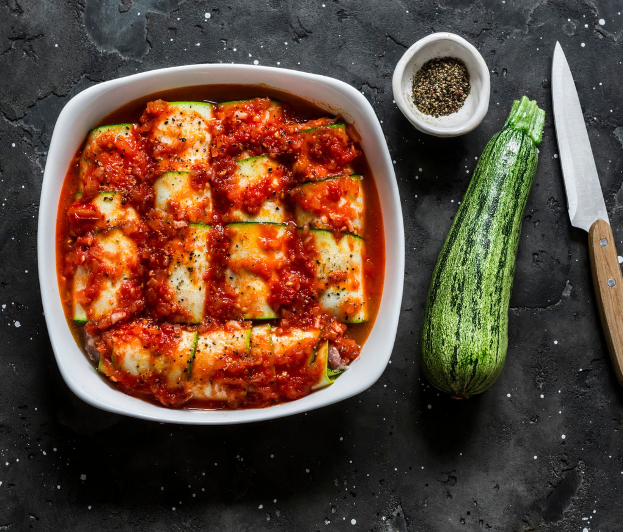 Raw Zucchini Cannelloni with Romesco Sauce near a zucchini and a knife