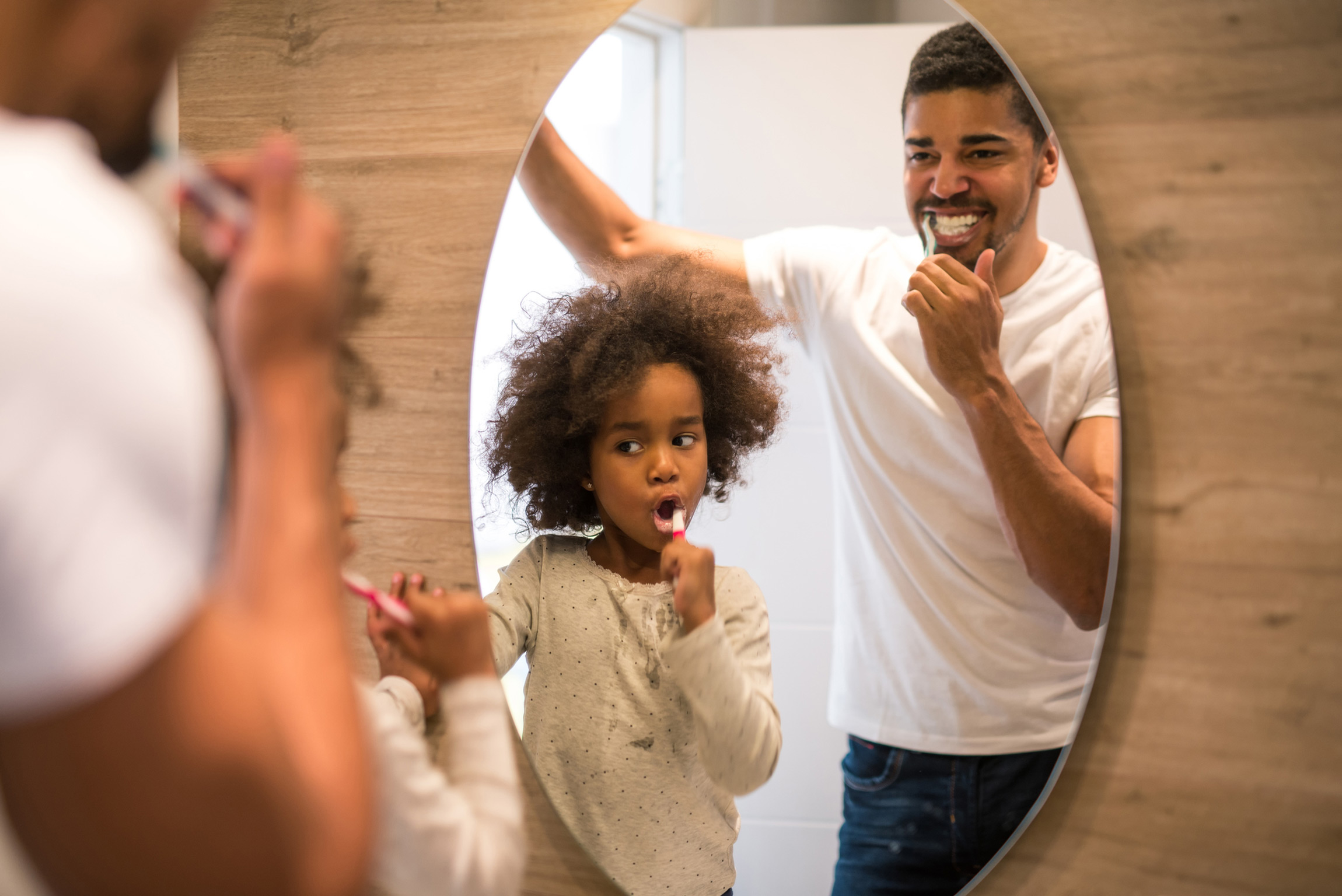 Father and daughter brushing their teeth in a mirror