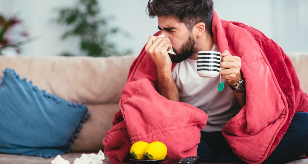 Man sick with a blanket, tea, lemons, and blowing his nose