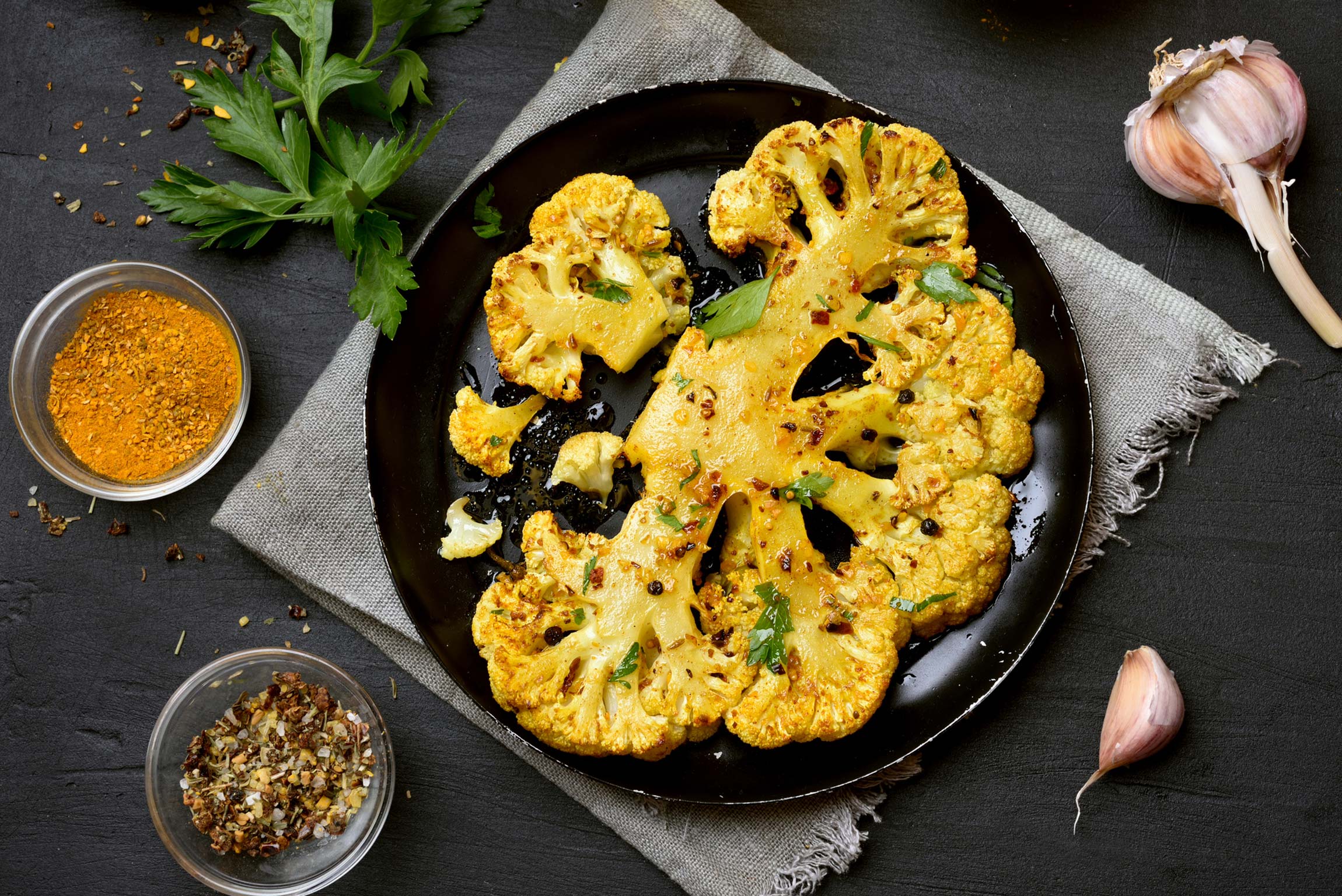 cauliflower steak on a plate, pictured with garlic, parsley and other dry seasonings