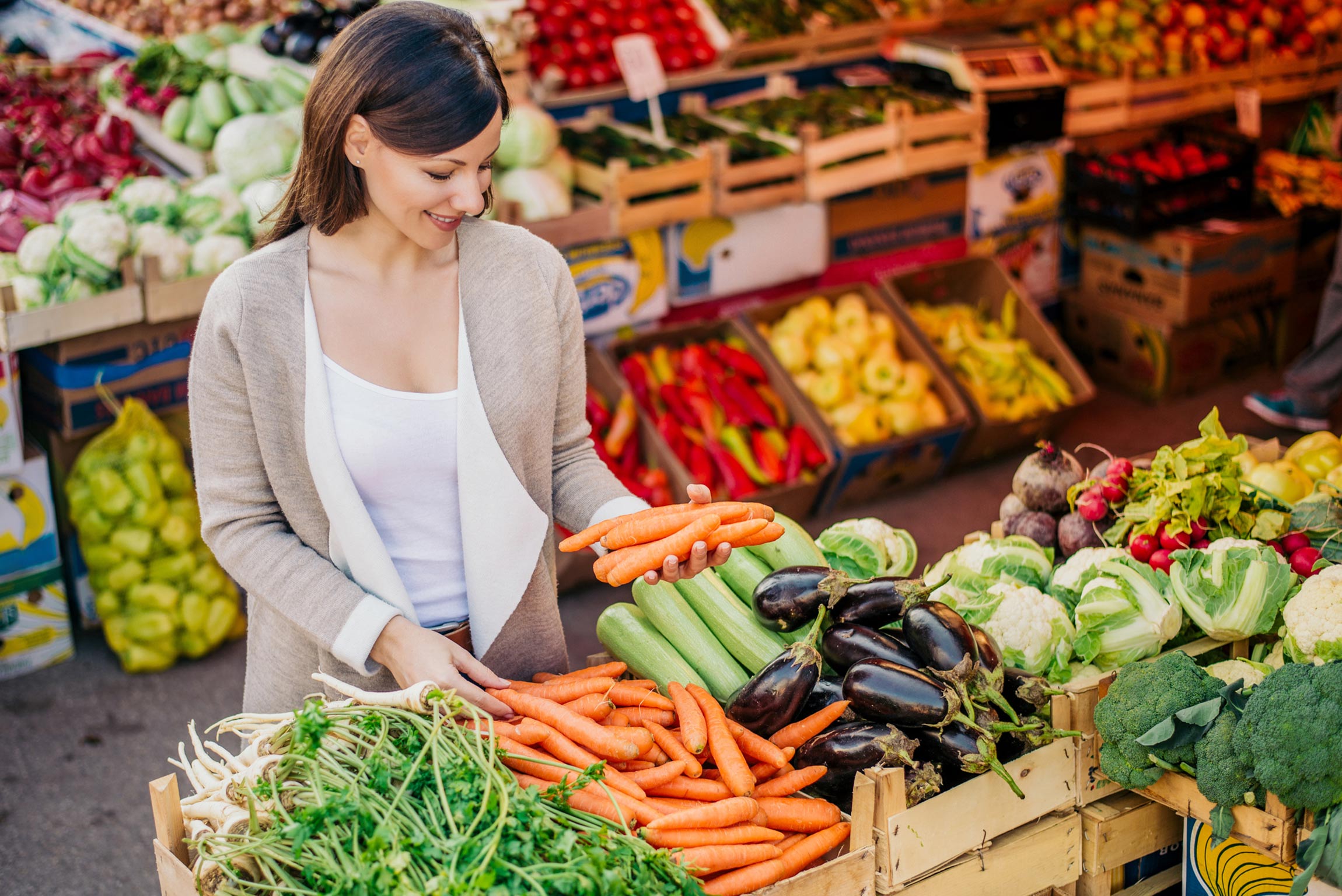 A woman shopping at a farmer's market holding carrots