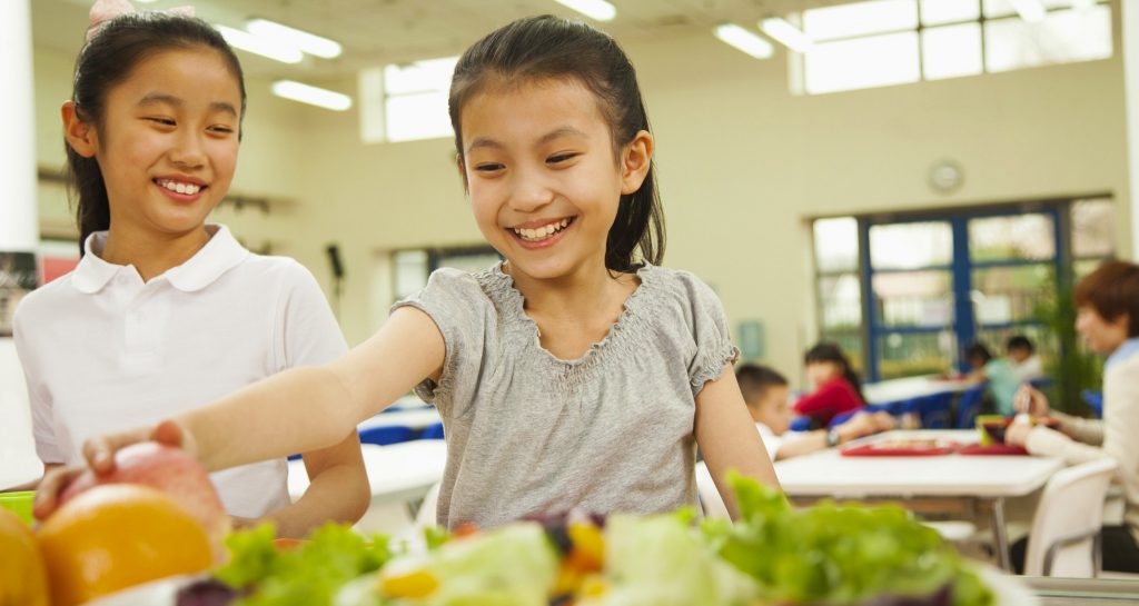 Young Asian student reaches for an apple for school lunch