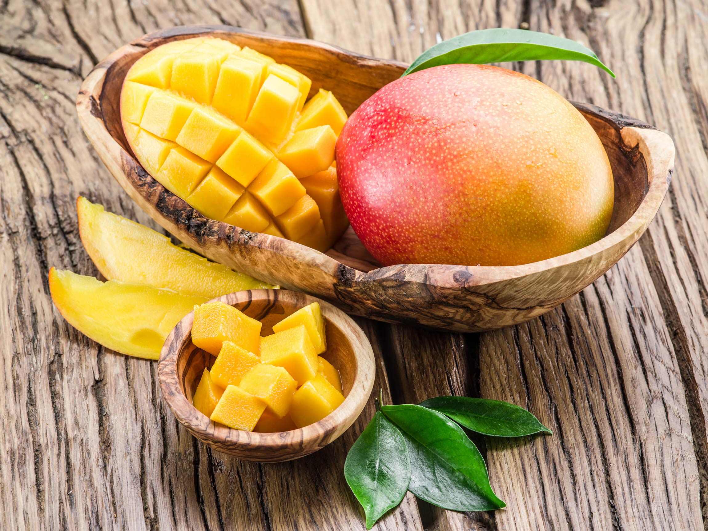 mango and cut mango in wooden bowl on table