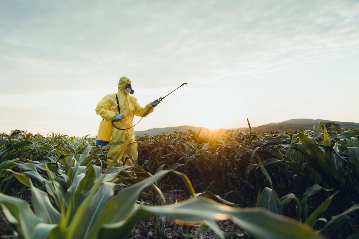 man in hazmat suit spraying crops with pesticides