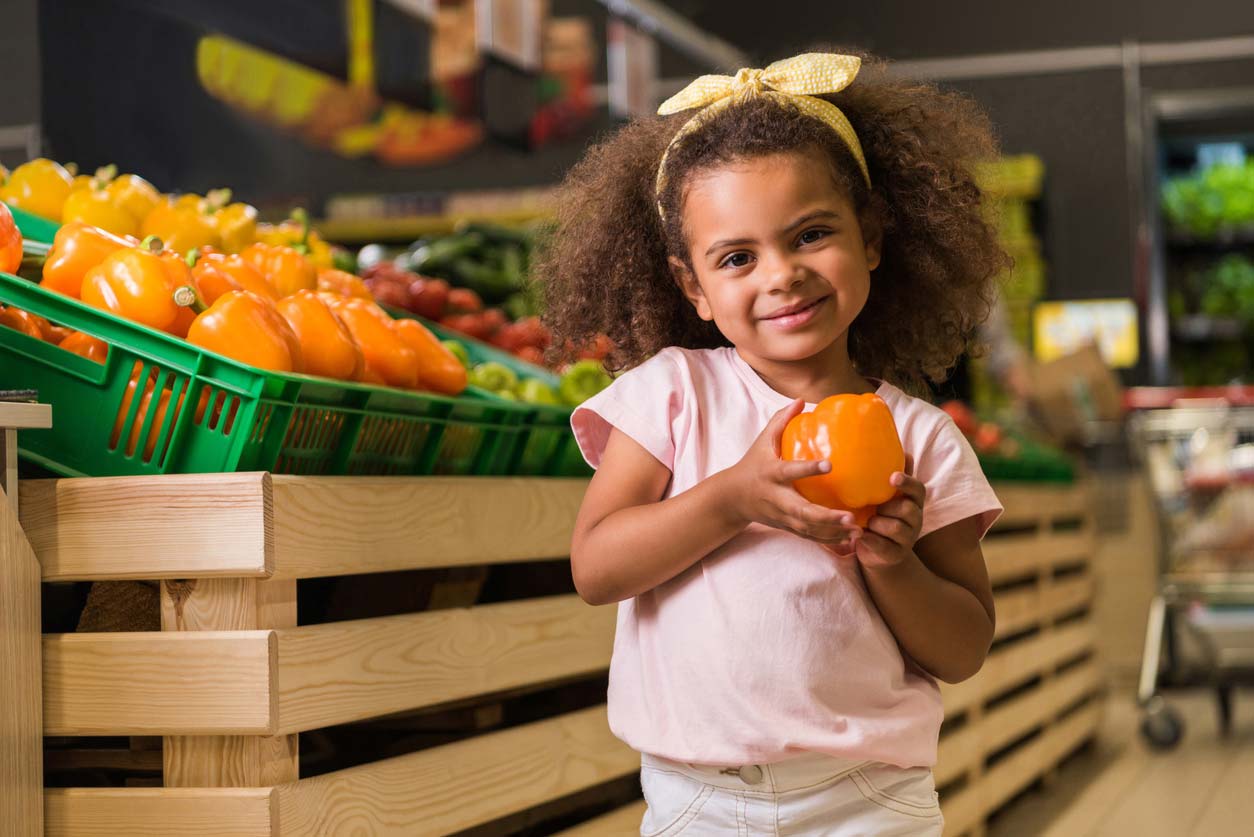 little girl holding bell pepper in grocery store