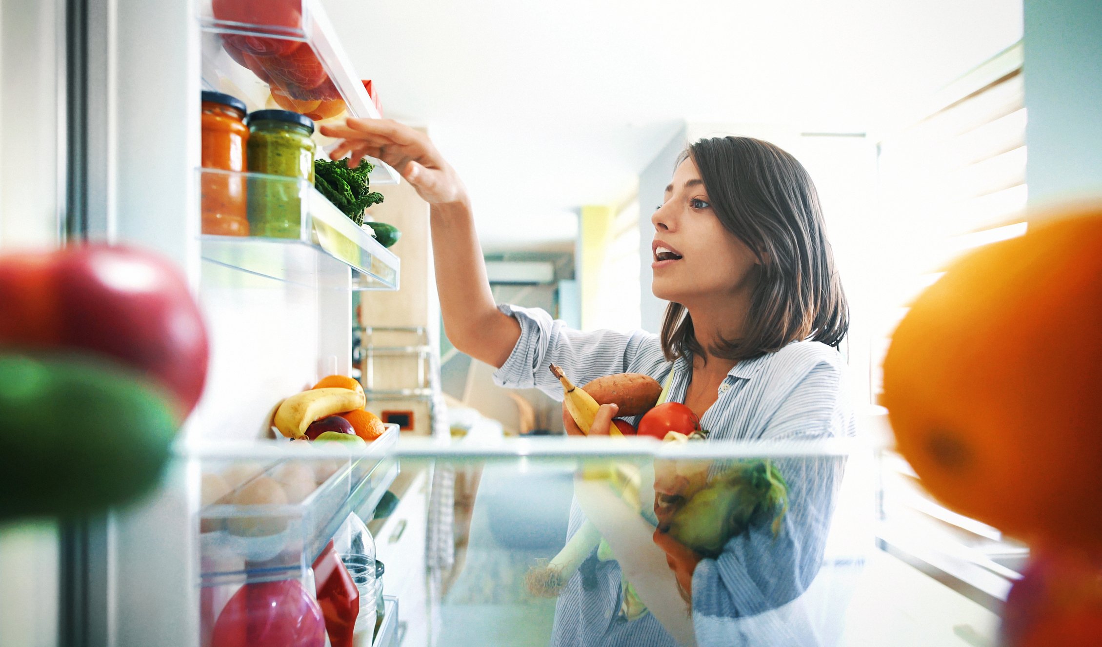 Woman picking up some fruits and veggies from the fridge