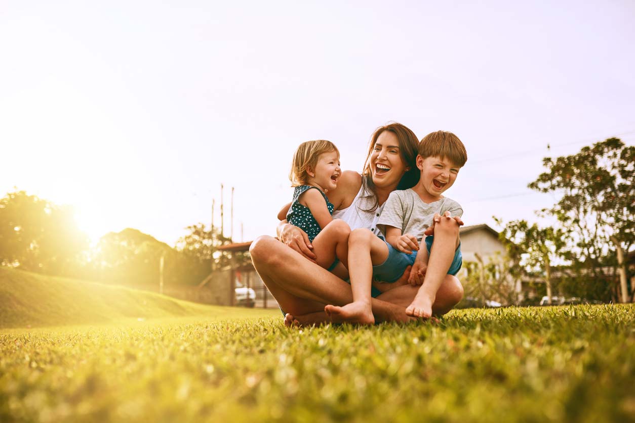 Mother laughing with two children on the grass