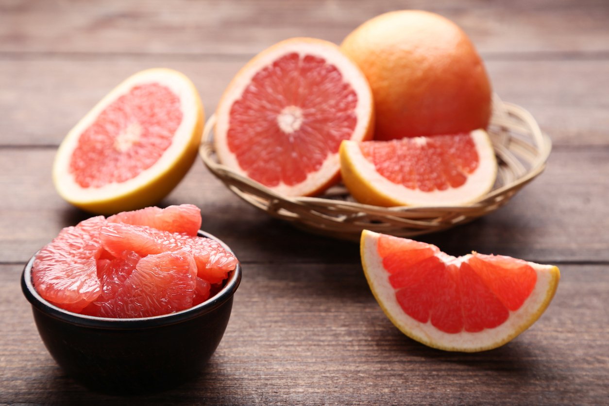 Ripe grapefruits in basket and bowl on brown wooden table