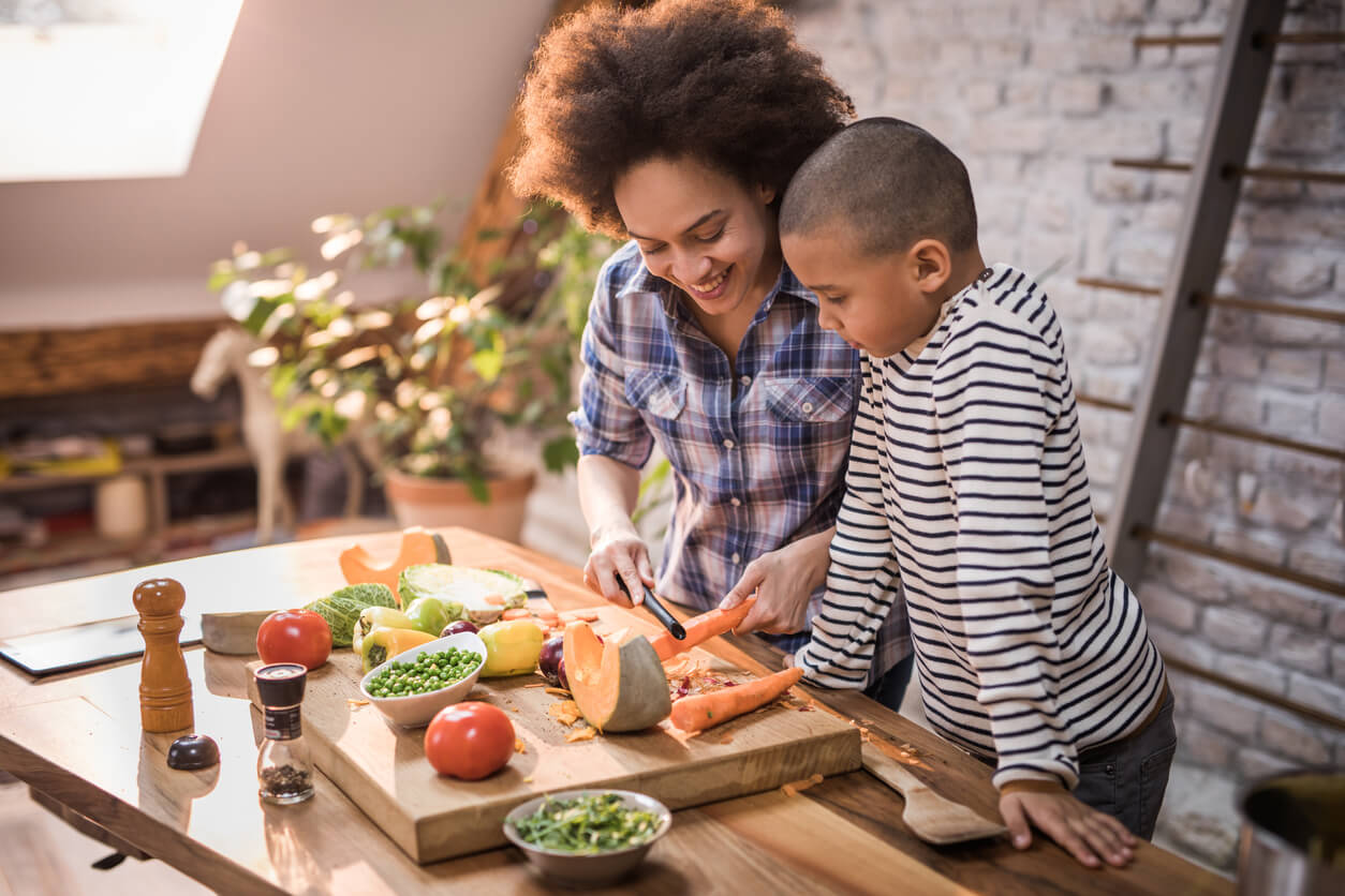 happy black mother teaching her son how to peel a carrot