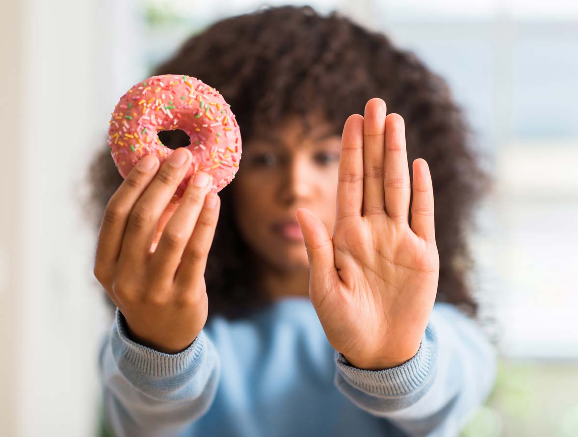 Woman holding up donut and hand to not eat it