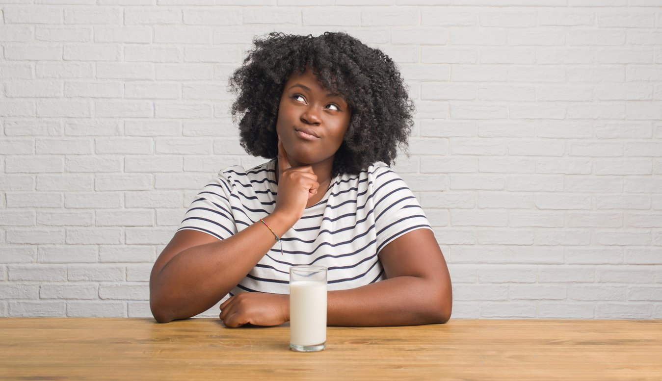 Young african american woman sitting on the table drinking a glass of milk serious face thinking about question, very confused idea