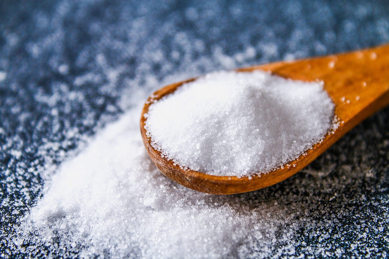 crystals of shallow salt in a scoop spoon on a dark grey table background