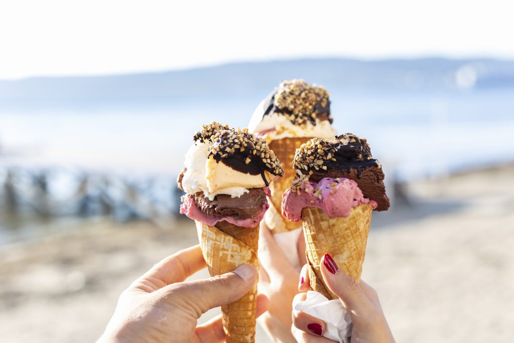 Three people hold up their ice creams together on the beach