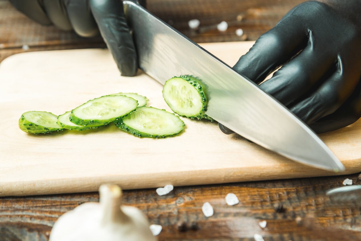 woman's hands cut a cucumber close to the tomatoes paprika and garlic