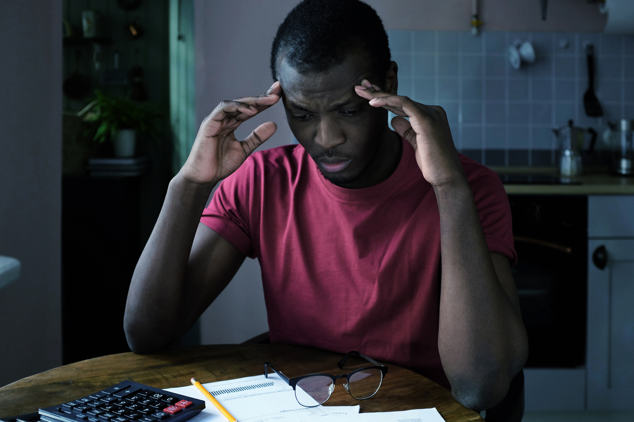 Unpaid debt problems. Young unhappy african american man trying to figure out details of bills, looking at papers from bank