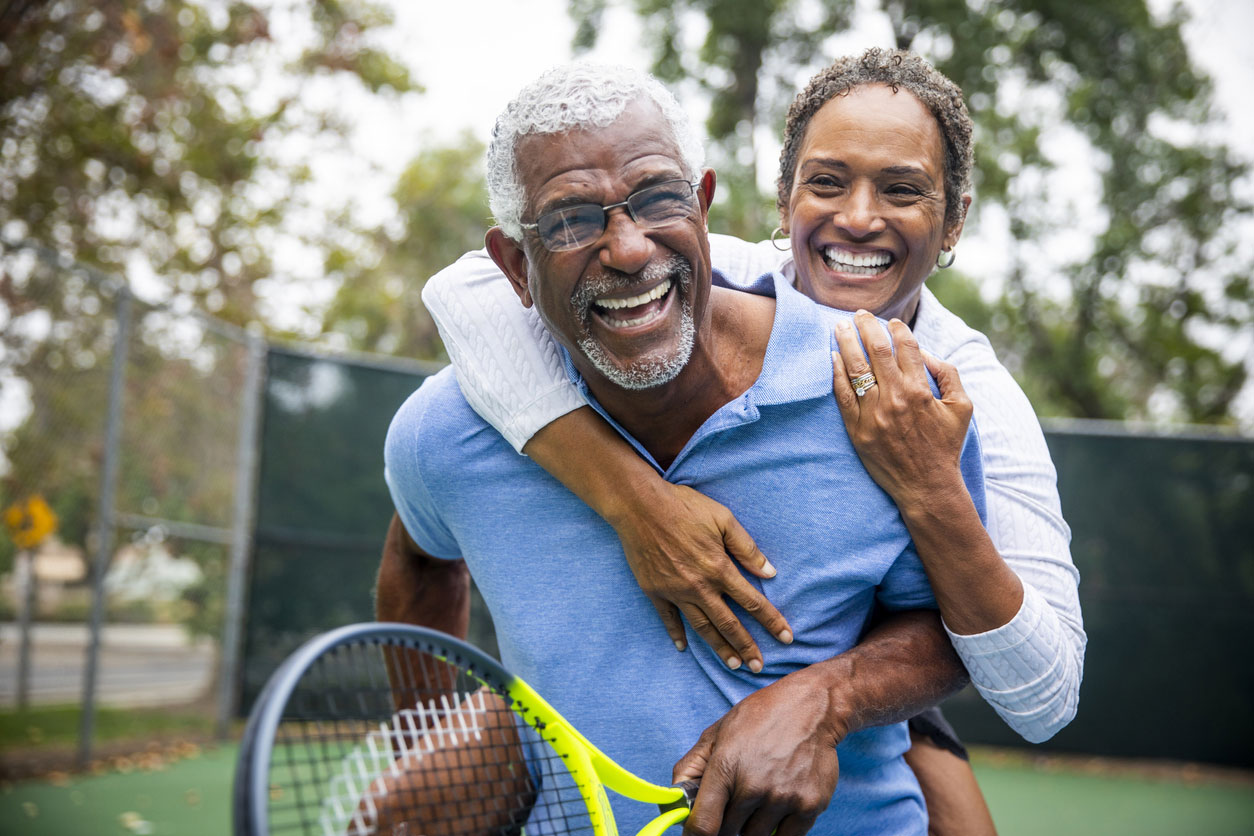 senior couple piggy-back on tennis court