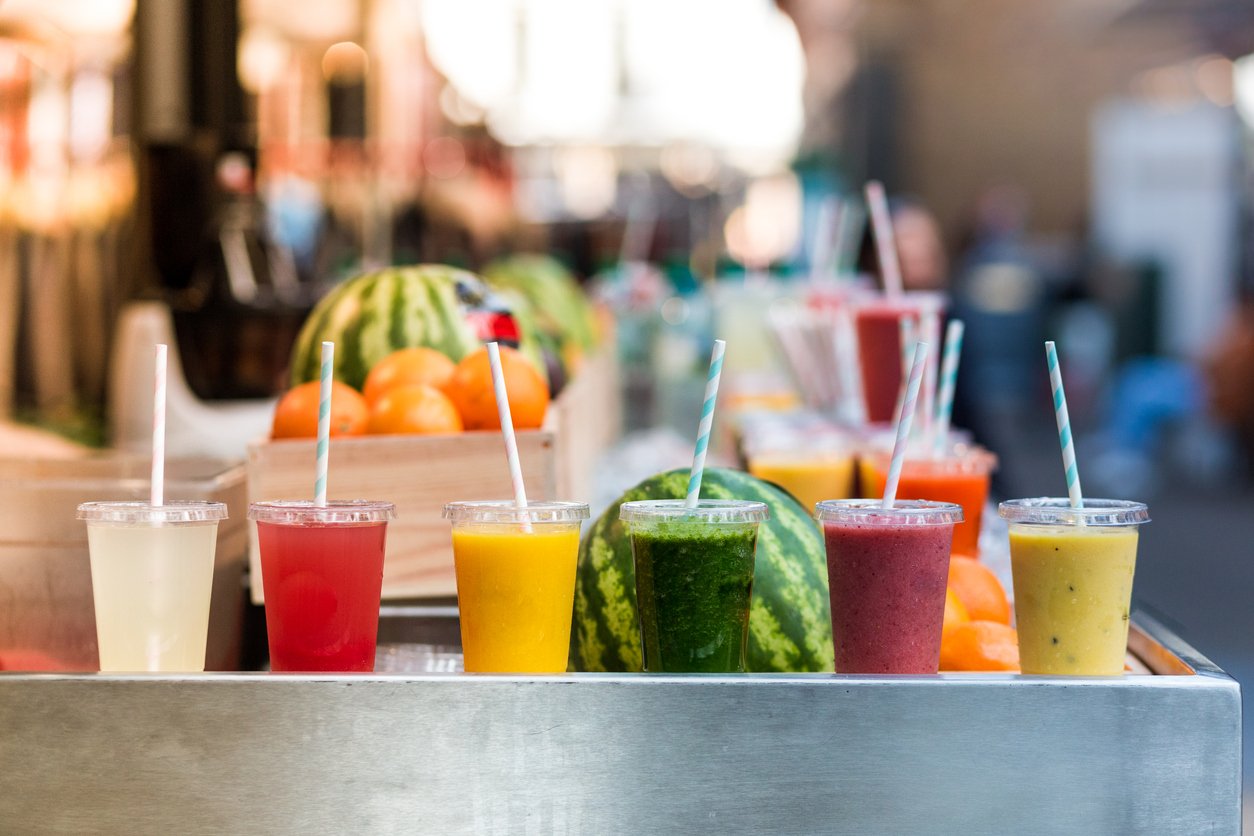 Close up of fresh fruit smoothies and juices in a row for sale on vegetarian market stall