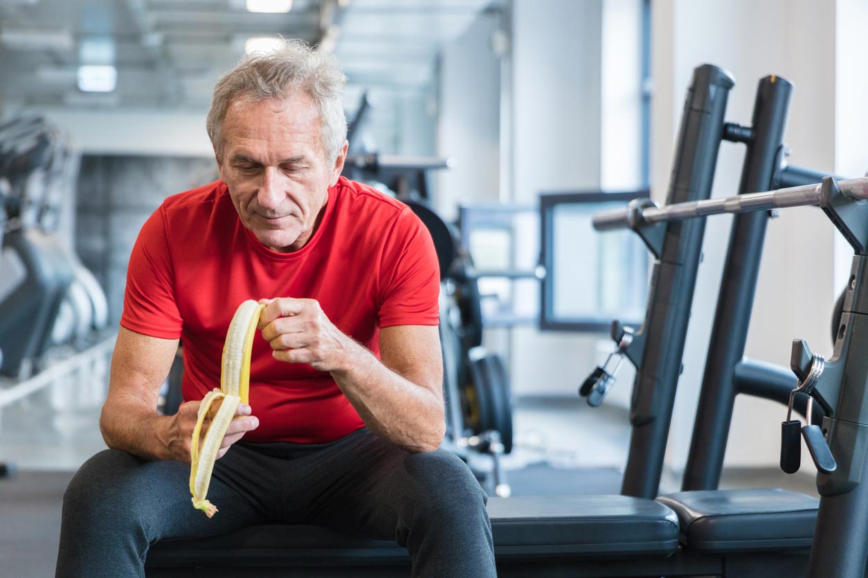 senior man eating banana in weight room