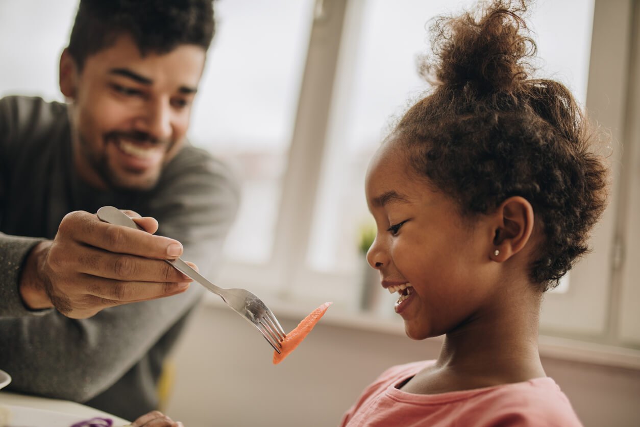 happy black girl being fed with a carrot by her father