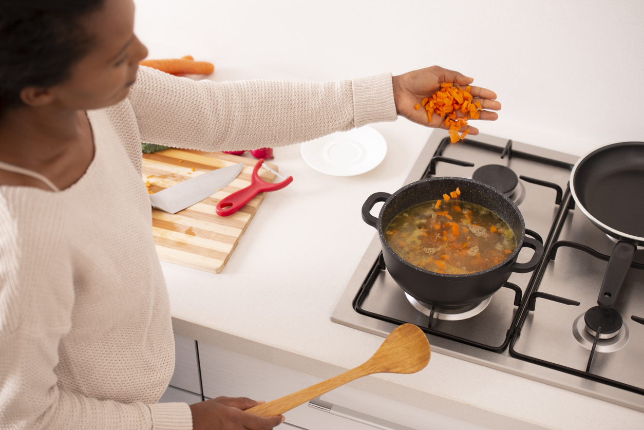 Woman bring the stock back to a boil, adding chopped carrots to the soup.