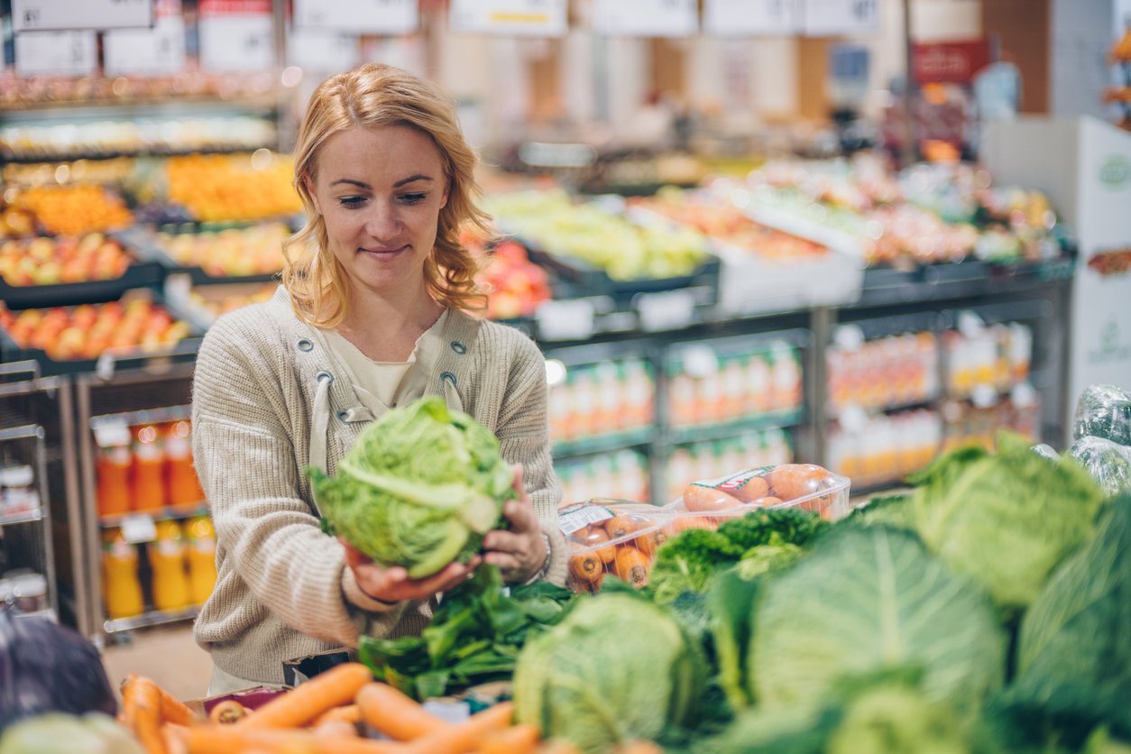 Young smiling woman buying cabbage in supermarket.