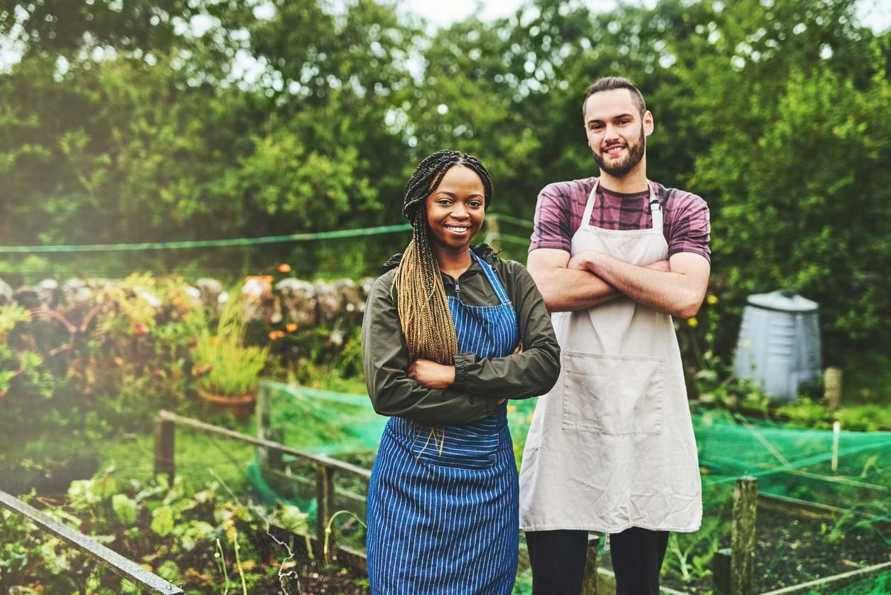 man and woman with crossed arms smiling in front of garden