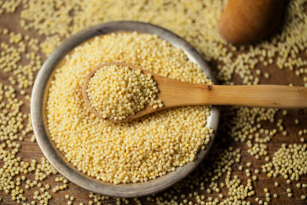 Millet groats in spoon above bowl