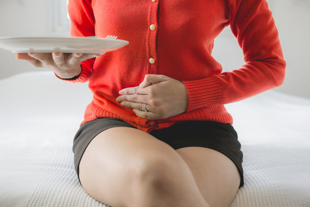 Woman holding her stomach and a plate of food