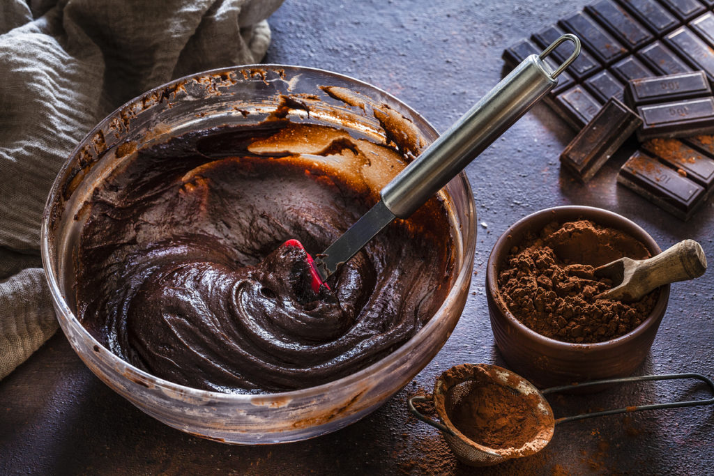 Bowl filled with chocolate batter, cocoa powder, chocolate bars, and cacao powder