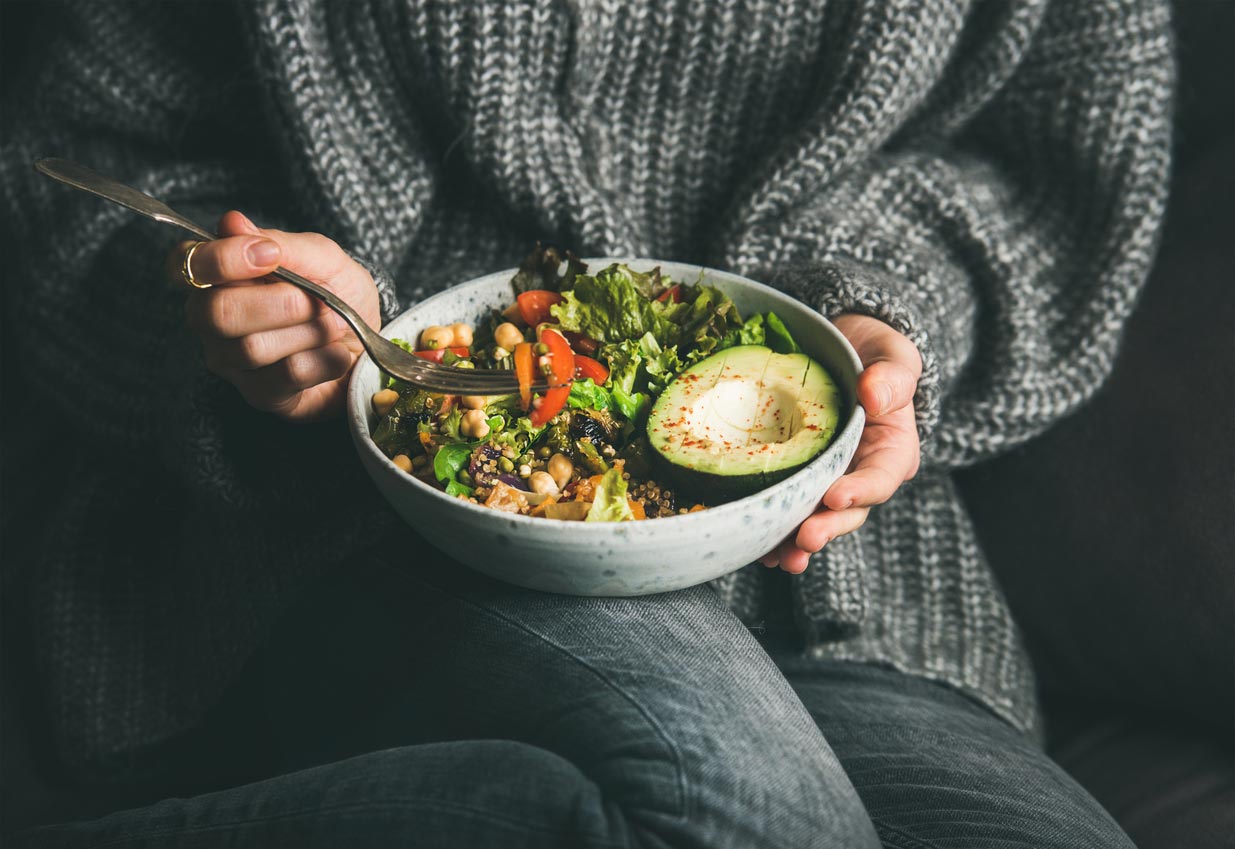 person in sweater holding bowl of greens