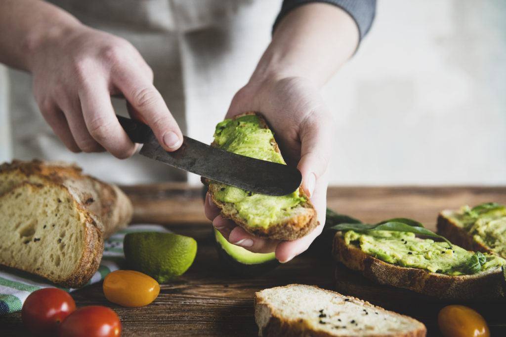 Spreading avocado on a piece of toast in the kitchen