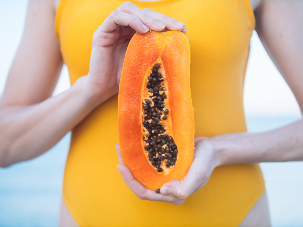 Woman in yellow swimsuit with exotic fruit papaya on the beach at sunset