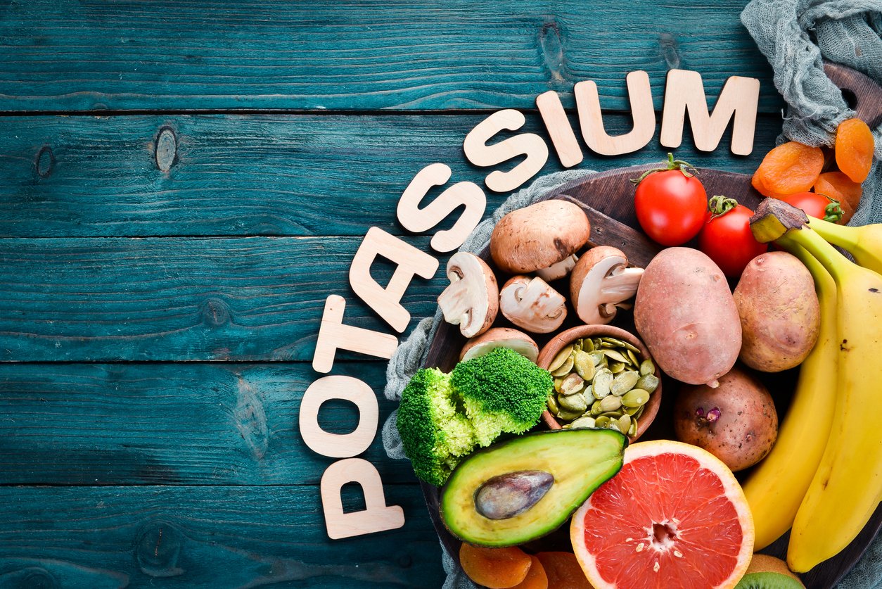 Foods containing natural potassium. K: Potatoes, mushrooms, banana, tomatoes, nuts, beans, broccoli, avocados. Top view. On a blue wooden background.