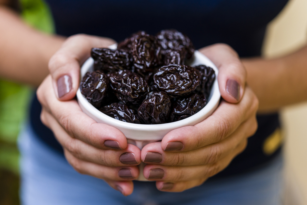 Manicured hands holding a white bowl of prunes