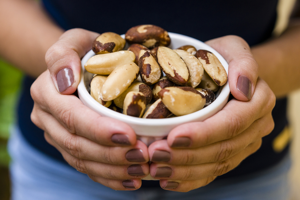 Brunette model hand holding white pot with brazilian nuts.