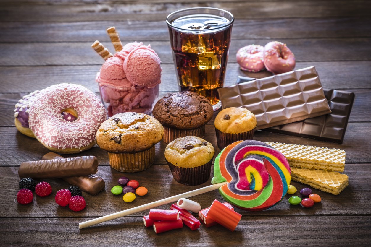 Assortment of products with high sugar level like candies, gummy candies, donuts, soda, chocolate, lollipop, wafers and cupcakes on rustic wooden table. Low key DSLR photo taken with Canon EOS 6D Mark II and Canon EF 24-105 mm f/4L