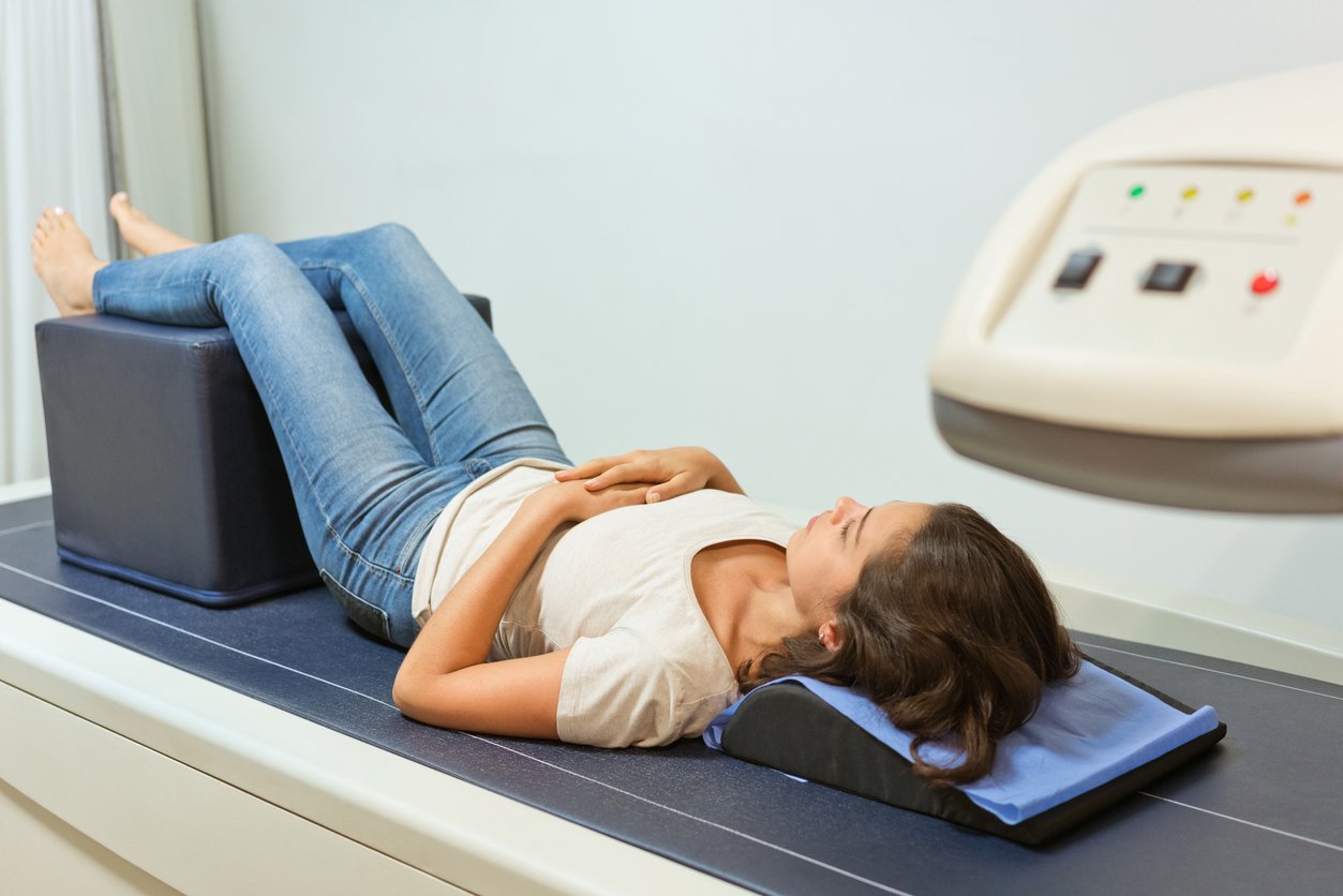 Full length of young woman going through bone density exam. Female patient is lying on densitometry machinery. She is at hospital.