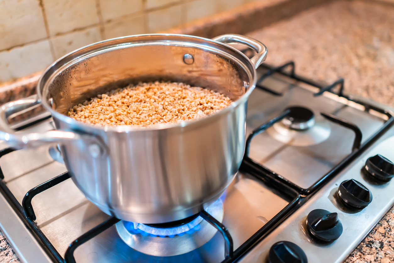 Closeup of buckwheat cooking in pot on gas stove in kitchen with blue natural gas flame and grain kasha cooked