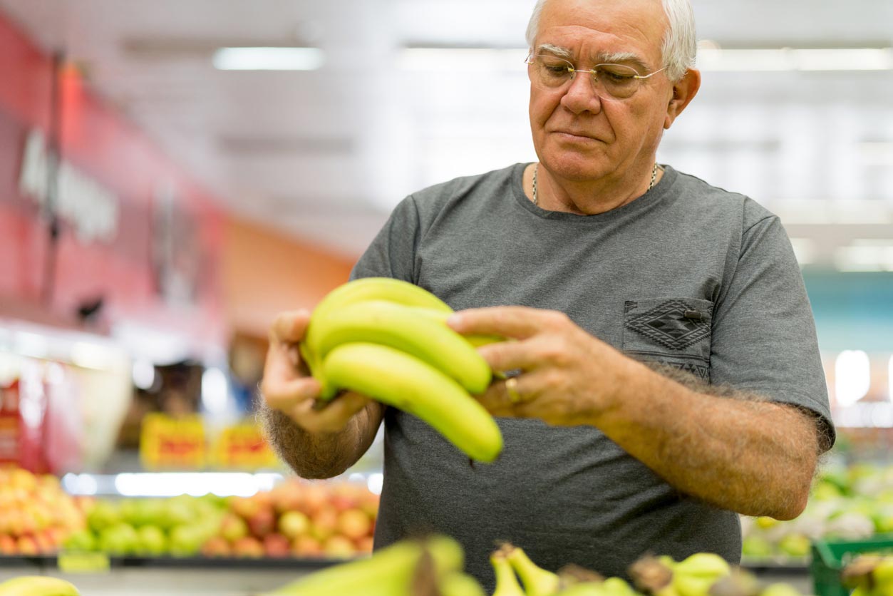 elderly man picking bananas produce section