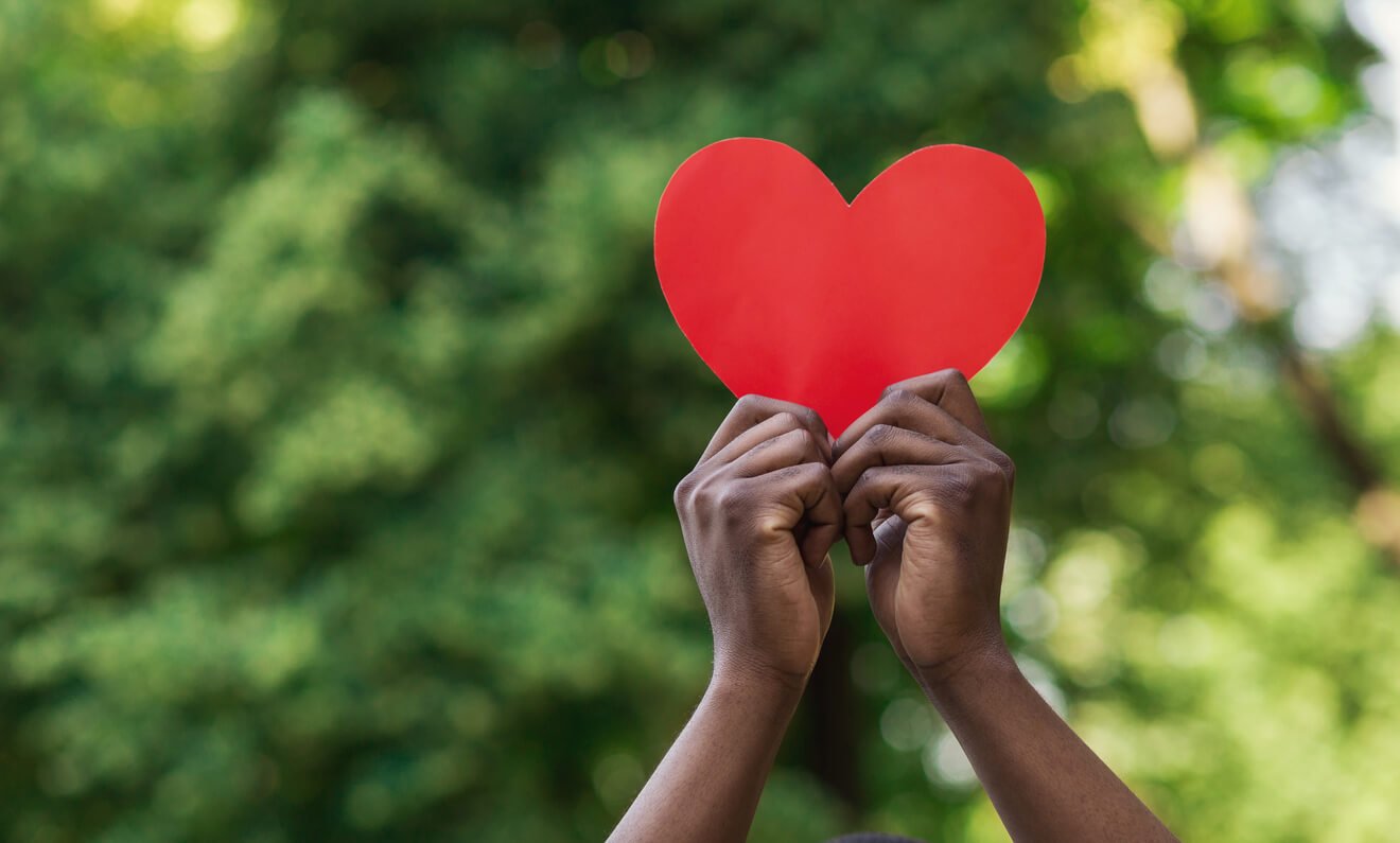 black hands holding red paper heart on green background