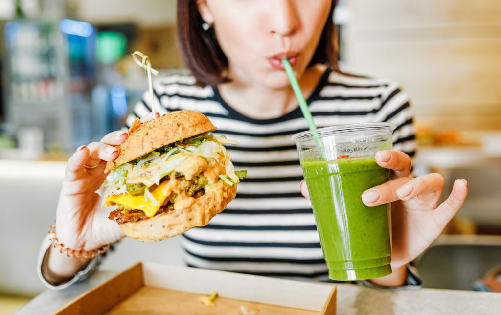 A young woman drinks green smoothies and eats a burger in a fast food restaurant