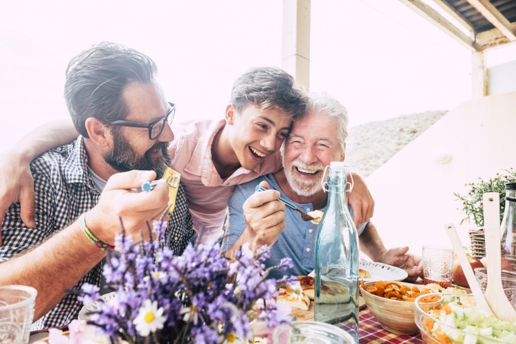 Three generations of Mediterranean men laughing during a meal