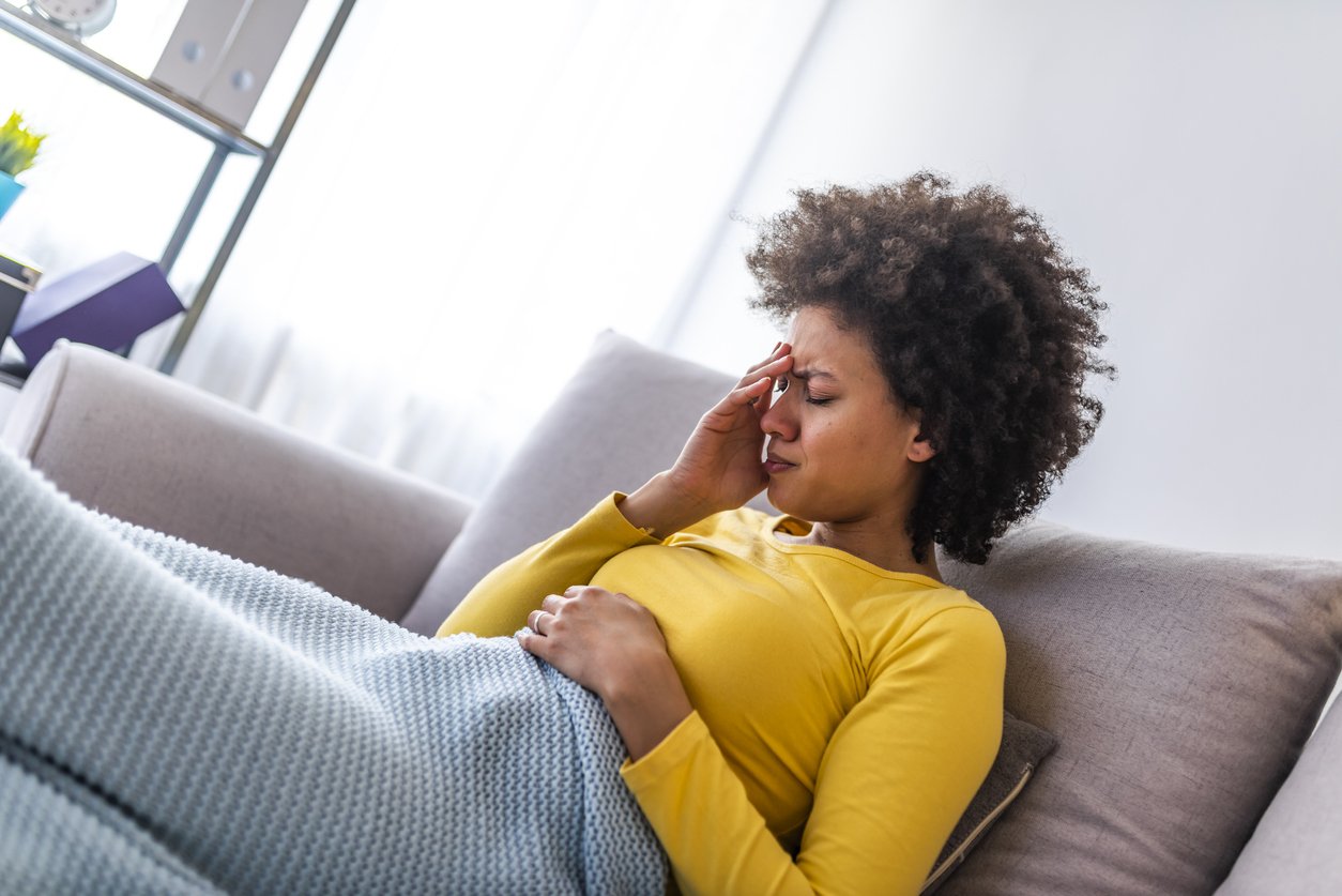 Young woman sitting on a couch, holding her head, having a strong headache