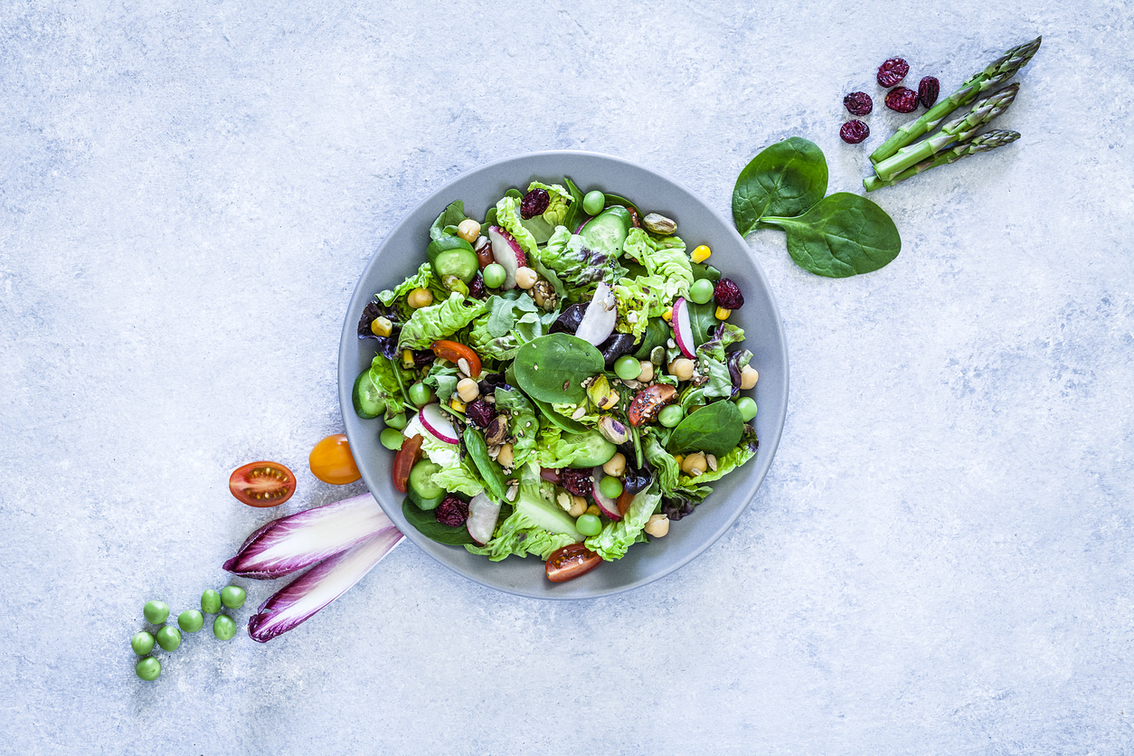 Vegan food: top view of a fresh organic multi colored vegetables salad shot on dark brown abstract background. The salad is in a gray plate and fresh ingredients like lettuce, green peas, parsley, pumpkin seeds, spinach, tomatoes, pistachios and asparagus are out of the plate placed directly on the background. Predominant colors are green and brown. Low key DSRL studio photo taken with Canon EOS 5D Mk II and Canon EF 100mm f/2.8L Macro IS USM.