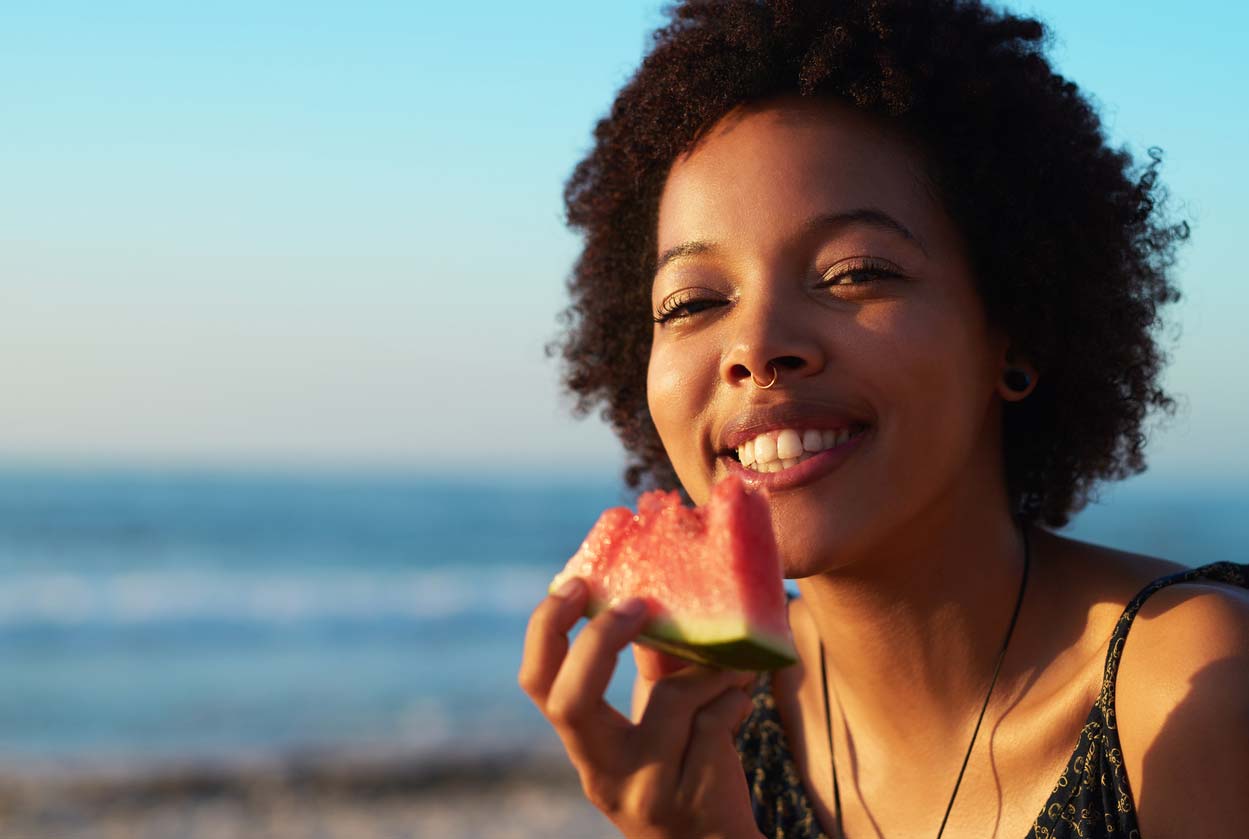 woman eating a summer food favorite - watermelon - at beach