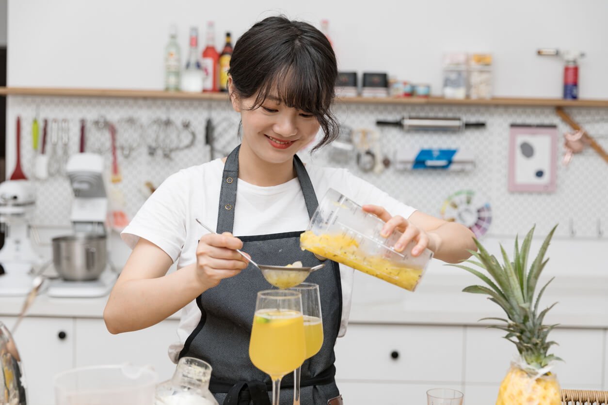 a smiling young chinese female pouring filtered juice into a glass in her kitchen 