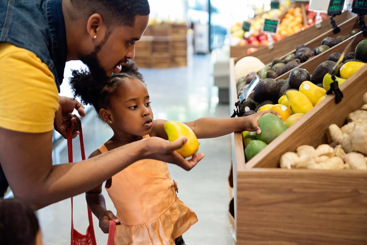 father and daughter picking out mangoes from supermarket