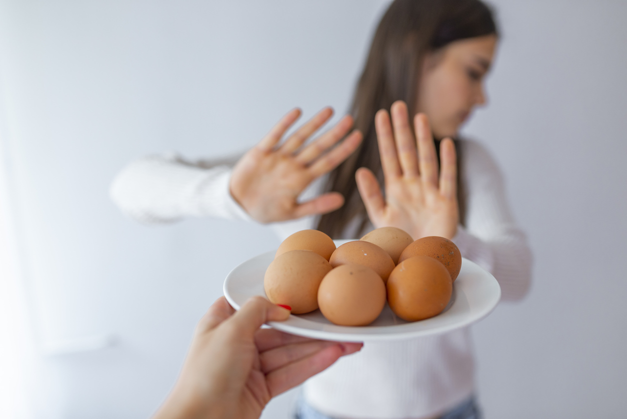Woman refusing to eat eggs. Egg Free Affected Allergy Banned Restriction. Young beautiful woman holding fresh egg at home with open hand doing stop sign with serious and confident expression